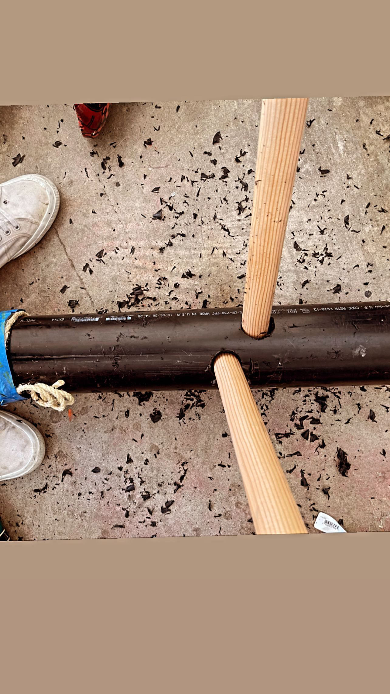 The PVC pipe on the workshop floor with two wooden dowels driven through it forming a crossbar.