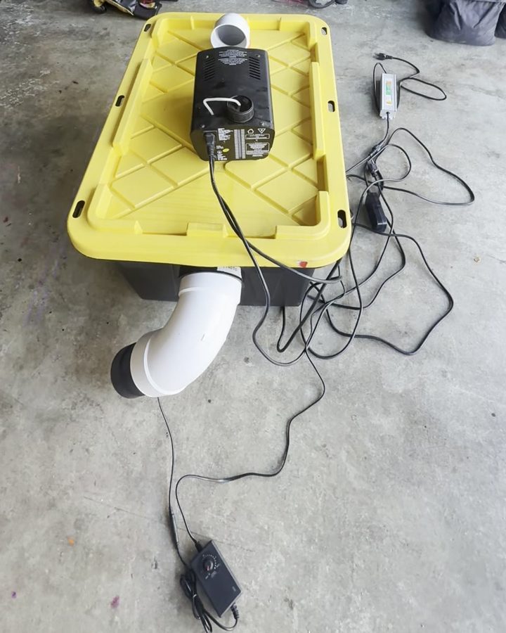 The finished fog chiller: black tote with a yellow lid, a fog machine on top, a white elbow out the side with an inline fan, and a speed knob on the floor