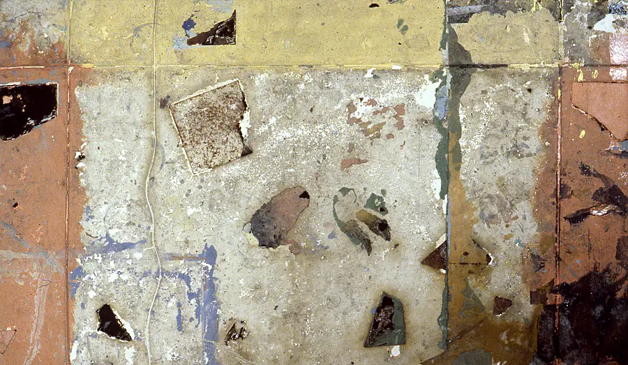 Patchwork surface of ochre, terracotta and cream paint with embedded dark fragments and a thin cord.