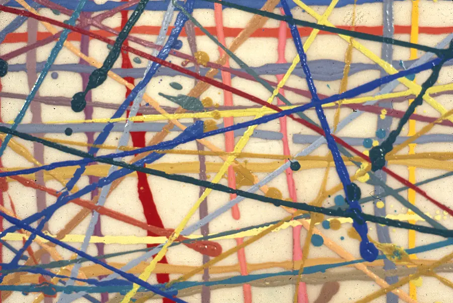 Detail of poured lines of red, blue, yellow and green paint crossing a cream ground.