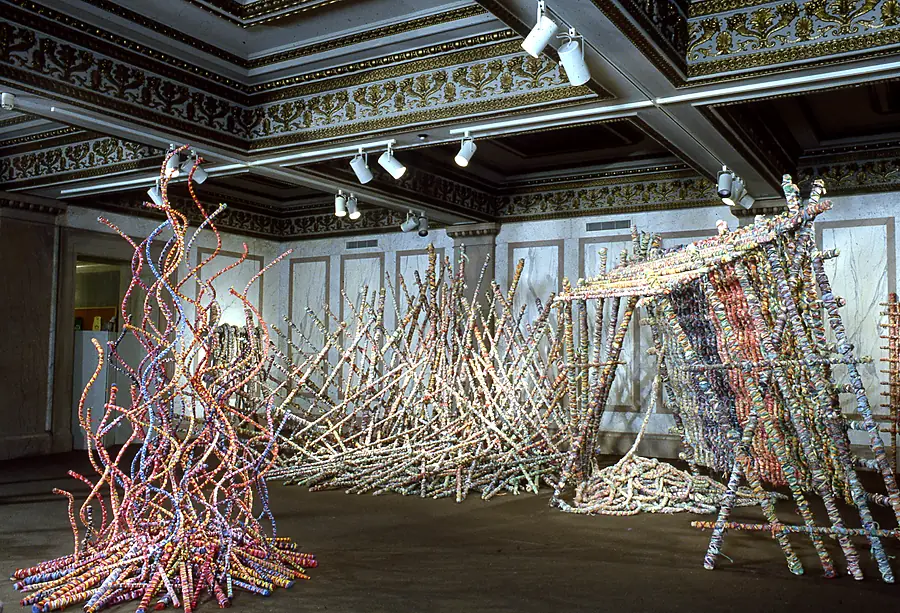 Tall curving wrapped rods, a field of leaning poles and a pole-framed tent in a hall with a gilded ceiling.
