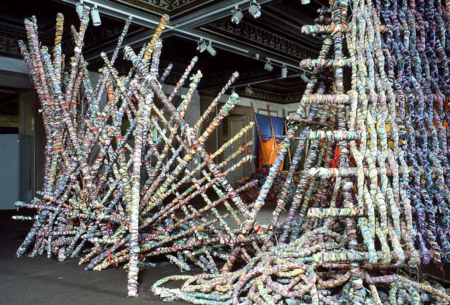 Large lattice of wrapped poles leaning against a ladder-like frame in a hall with an ornate ceiling.