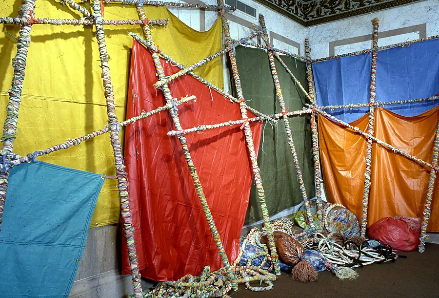 Pole lattices holding yellow, red, olive, blue and orange fabric panels, with coils of wrapped rope on the floor.