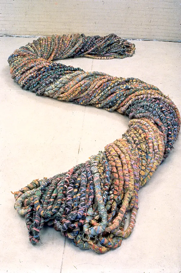 S-shaped floor sculpture of twisted ropes wrapped in muted strips of cloth, seen from above.