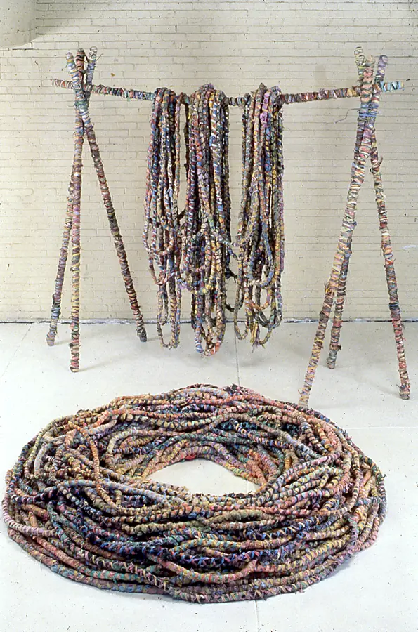 Wooden frame hung with loops of wrapped rope above a large circular coil of wrapped rope.