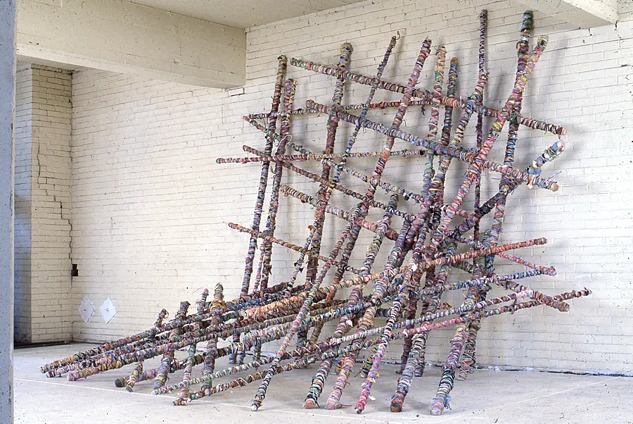 Large lean-to lattice of wrapped poles against a white brick wall.