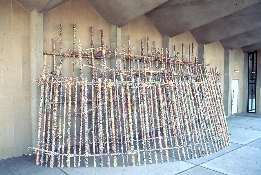Curved row of upright wrapped poles joined by horizontal rails, standing in a concrete hall.