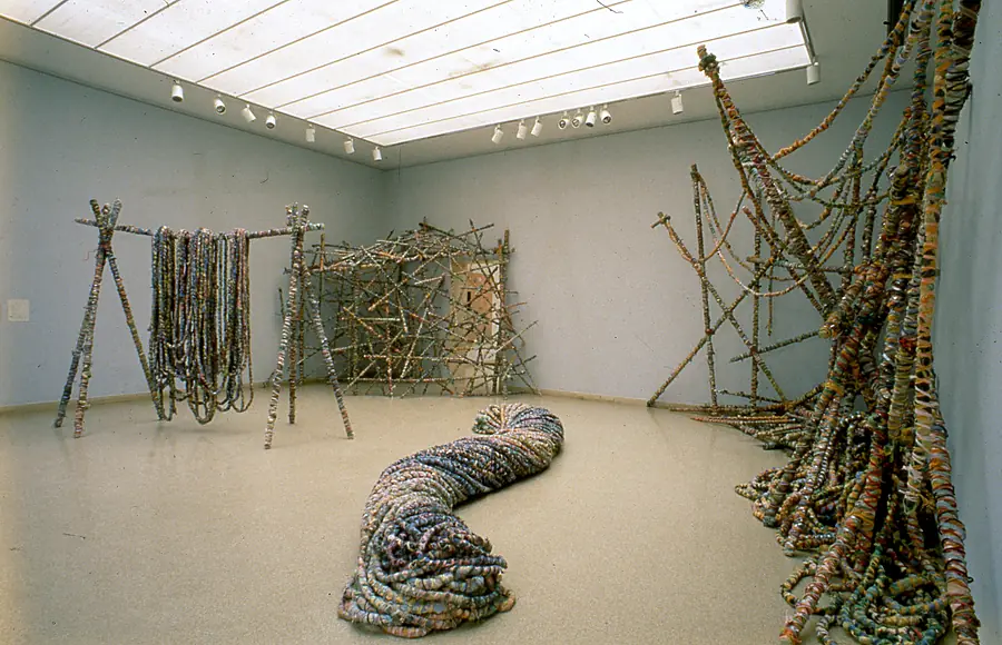 Skylit gallery holding a long rope serpent, a frame hung with wrapped ropes and lattices of wrapped poles.