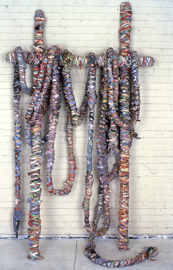 Wrapped ropes looped over a crossbar and hanging against a white brick wall.