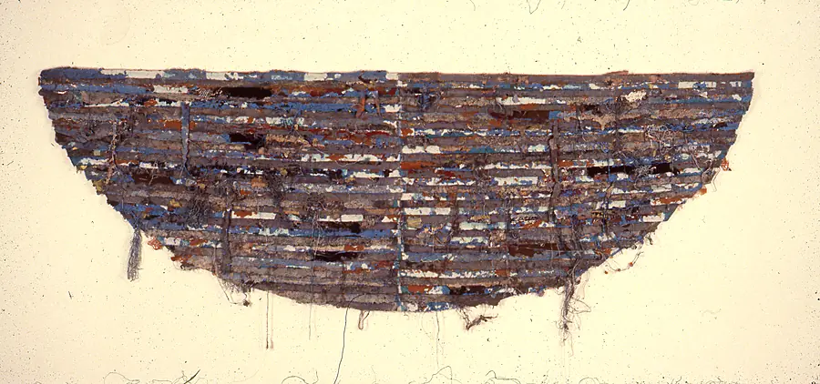 Half-round wall piece of stacked blue, gray, rust and white strips with threads trailing from the lower edge.