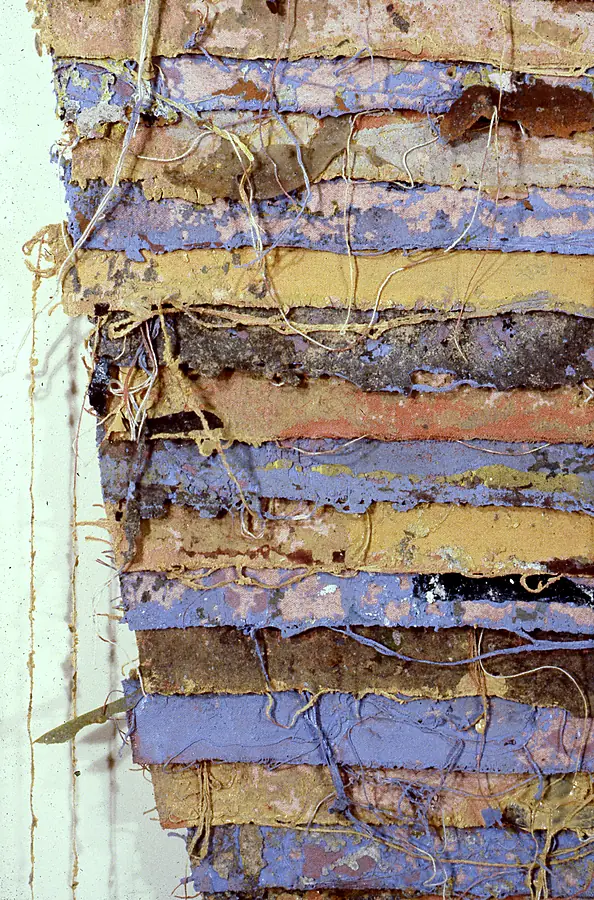 Detail of stacked canvas strips in lilac, ochre, rose and brown with cord laced across them.