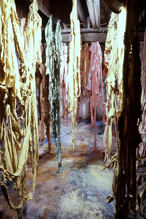 Dyed fabric strips hanging from studio beams above a paint-stained floor.