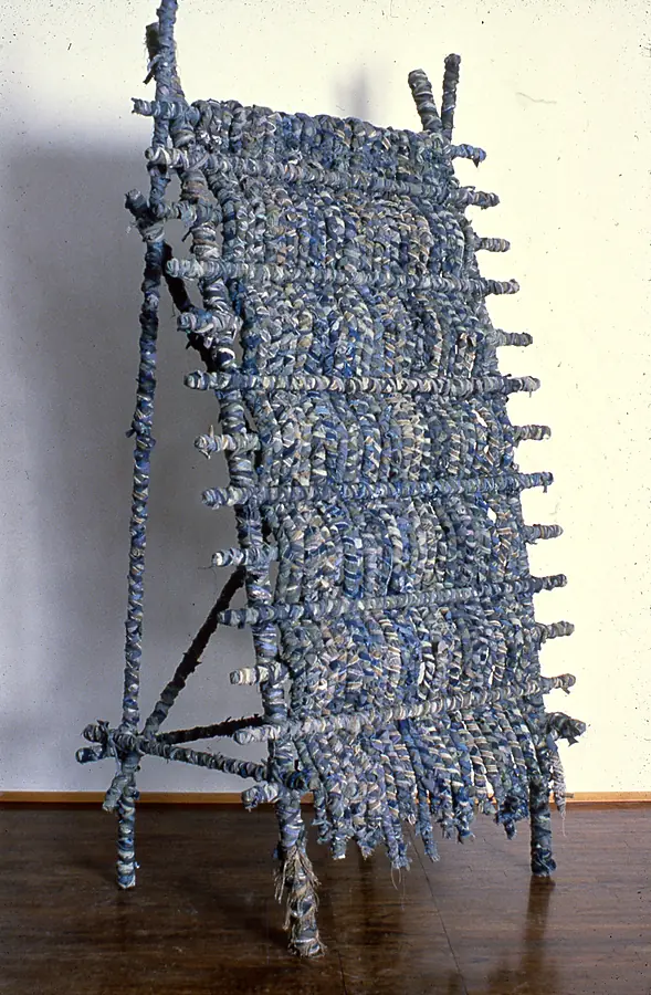 Woven blue panel on a leaning pole frame, with frayed strips trailing at the bottom.