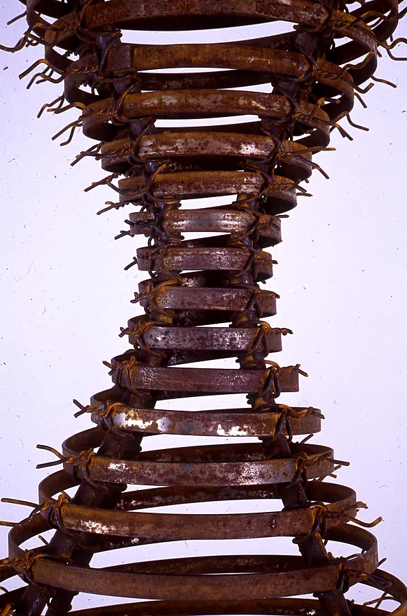 Detail of stacked rusted metal bands bound with wire barbs.
